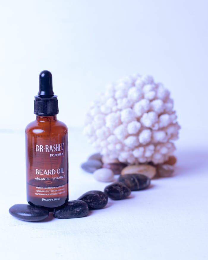 Brown glass beard oil bottle with stones and coral on white background.